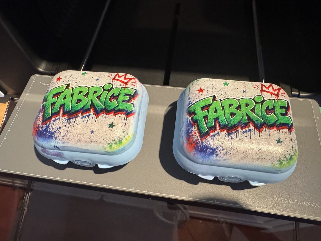 Zwei hellblaue 3D-gedruckte Dosen, im UV-Direktdruck mit einem farbigen Graffiti-Schriftzug „Fabrice“ veredelt